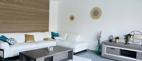 A modern living room with a white sofa, a dark coffee table, and a TV unit.