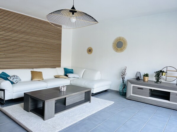 Un salón moderno con un sofá blanco, una mesa de centro oscura y un mueble para la televisión.