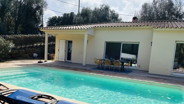 Una piscina con sillones de descanso, un porche cubierto con sillas amarillas y un muro de piedra al fondo.