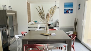 Un comedor con una mesa de madera, sillas rojas y blancas, un jarrón con plantas secas y un cuadro en la pared.