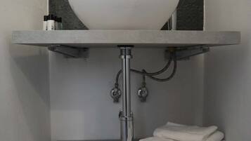 Ein Badezimmer mit weißem Waschbecken, grauen Fliesen und einem Handtuchhalter mit gefalteten Handtüchern.