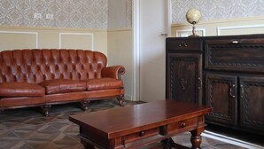 A room with a brown leather sofa, a wooden table, and a dark wooden cabinet. - Camera Deluxe (Recetto)