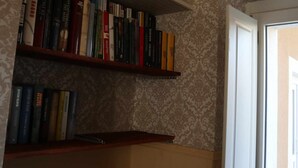 Ein Zimmer mit Wandpapier mit Muster, einem Bücherregal mit verschiedenen Büchern und einer Tür, die in ein weiteres Zimmer führt.