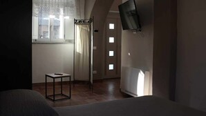 Une pièce comprenant un lit, une petite table, une fenêtre avec des rideaux, un radiateur et un téléviseur fixé au mur.