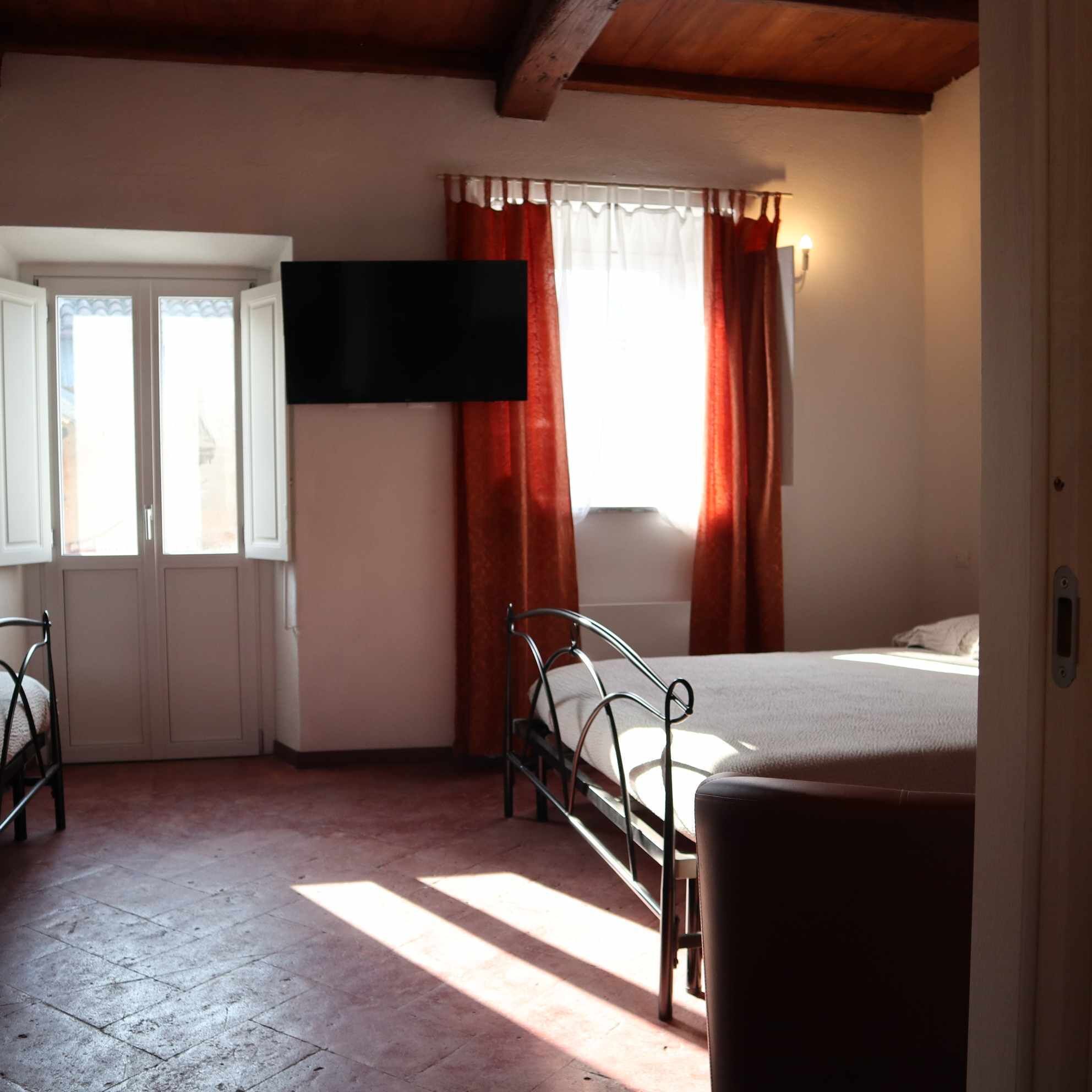 Ein Schlafzimmer mit Bett, Sessel, Fernseher und einem Fenster mit Vorhängen.