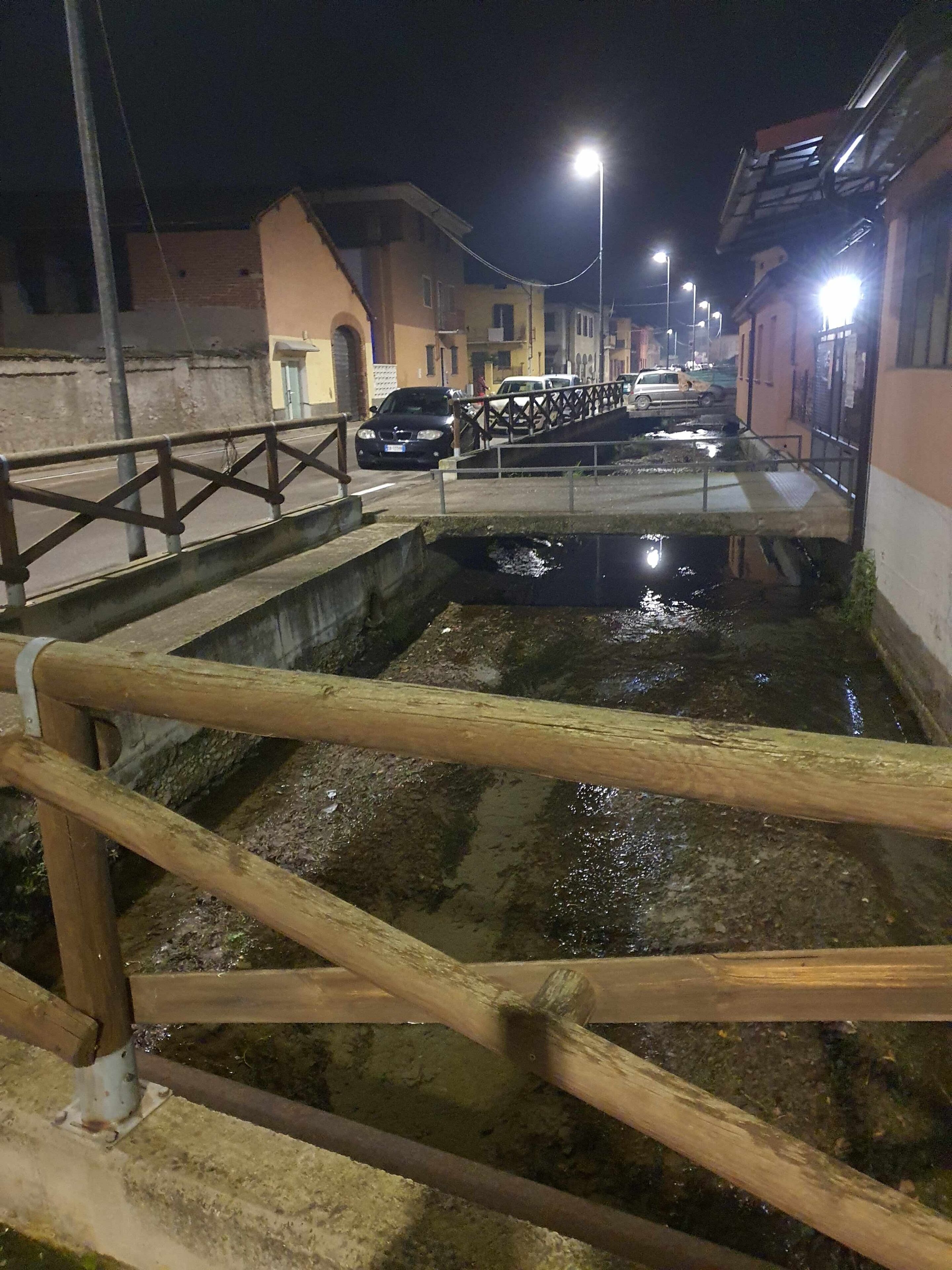 A narrow street with buildings on both sides, a wooden bridge, and streetlights.