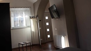 Une chambre avec un lit, un téléviseur fixé au mur, une fenêtre avec des rideaux et une petite table.