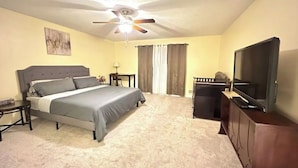 Ein Schlafzimmer mit einem Bett, einem Fernseher, einem Deckenventilator und Vorhängen.
