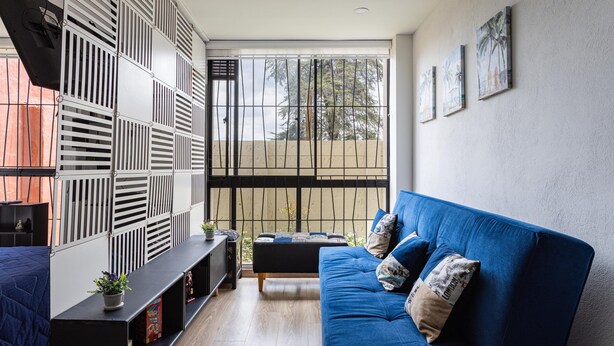 A modern living room with a blue sofa, a black entertainment unit, and a large window with a view of trees. - Loft, Historic Center, Bogotá (Bogotá)