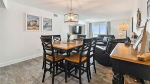 A dining area with a wooden table and chairs, a ceiling fan, and artwork on the walls.