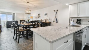A spacious kitchen with white cabinets, a marble countertop, and a dining area with wooden chairs and a table.