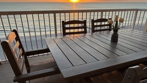 A wooden table with four chairs on a balcony overlooking the ocean at sunset.