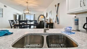 A modern kitchen with a double sink, white cabinets, and a dining area with a chandelier.