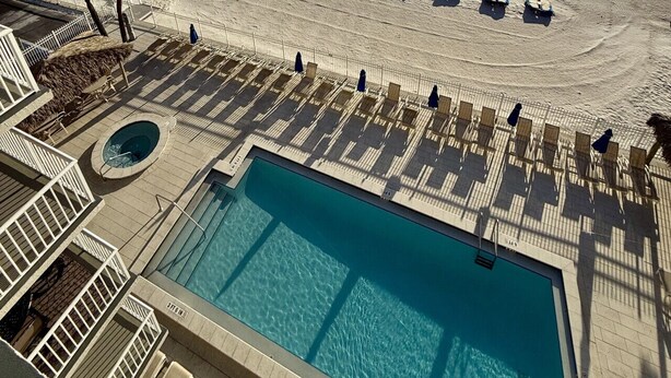 A pool area with lounge chairs and a view of the beach and ocean.