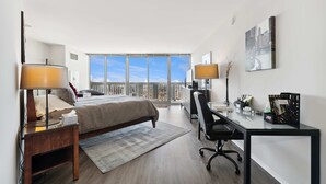 A modern hotel room with a bed, desk, and chair, large windows with a city view, and a small balcony. - 50th Floor Mag Mile Views, Balcony, Pool, Gym (Chicago)