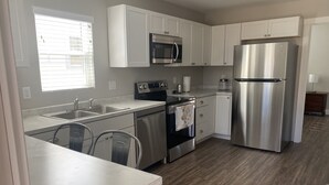 A modern kitchen with white cabinets, stainless steel appliances, a dishwasher, and a wooden floor. - Newly Renovated Charming Cottage, Occupancy 4   (Cedar Rapids)