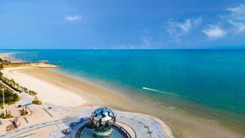 A coastal view with a beach, a fountain, and a clear sky.