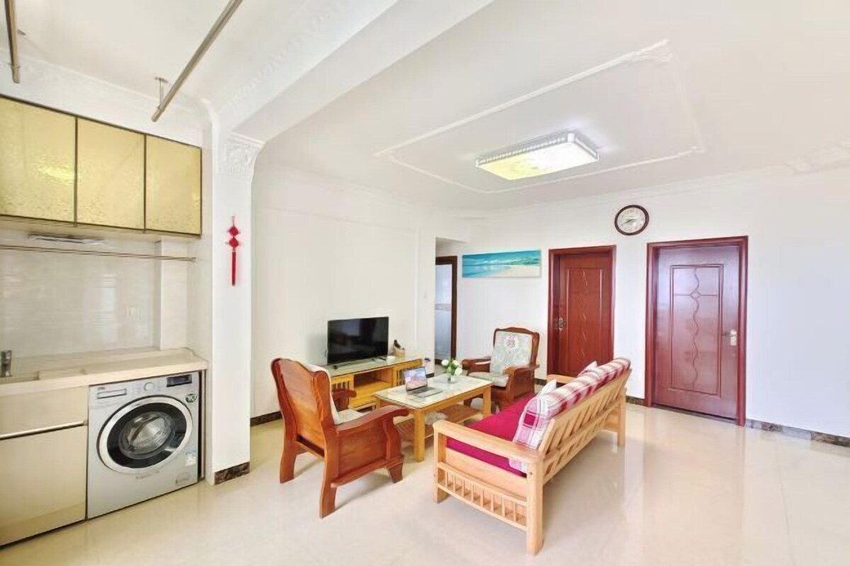 Un espacio habitable compacto con lavadora, una zona de comedor con sillas y mesa, sofá y televisión.