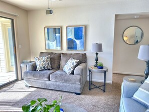 A living room with a grey sofa, two framed abstract paintings, a side table with a lamp, a small potted plant, and a round mirror on the wall. - Heated Pool/Hot Tub, Gorgeous, All New Furnishings (Branson)