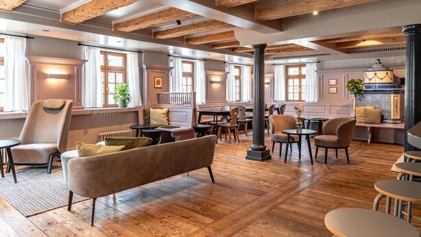 A spacious room with wooden beams, a large sofa, and multiple tables and chairs. - Hotel Deville Staufen (Staufen im Breisgau)