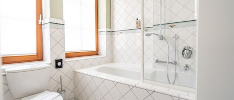 A bathroom with a toilet, a window, a bathtub, and a shower.