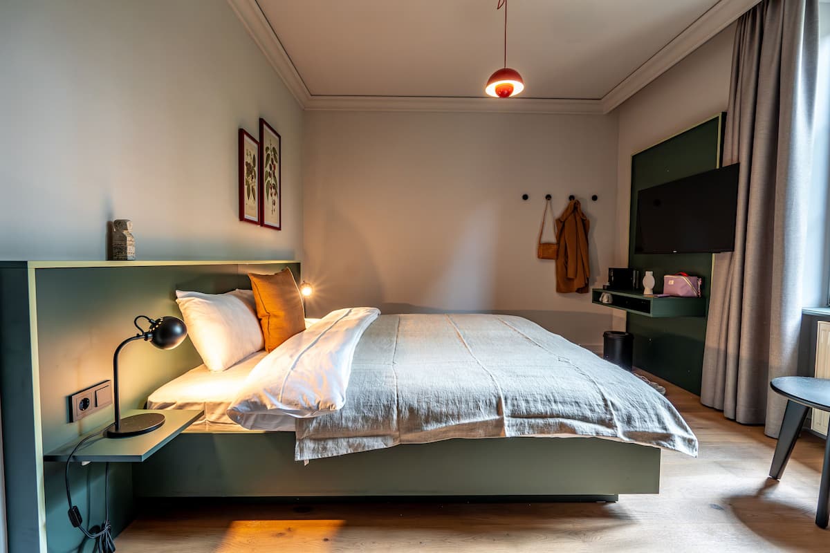Un dormitorio moderno con cama, mesita de noche, lámpara y televisor sobre un mueble.
