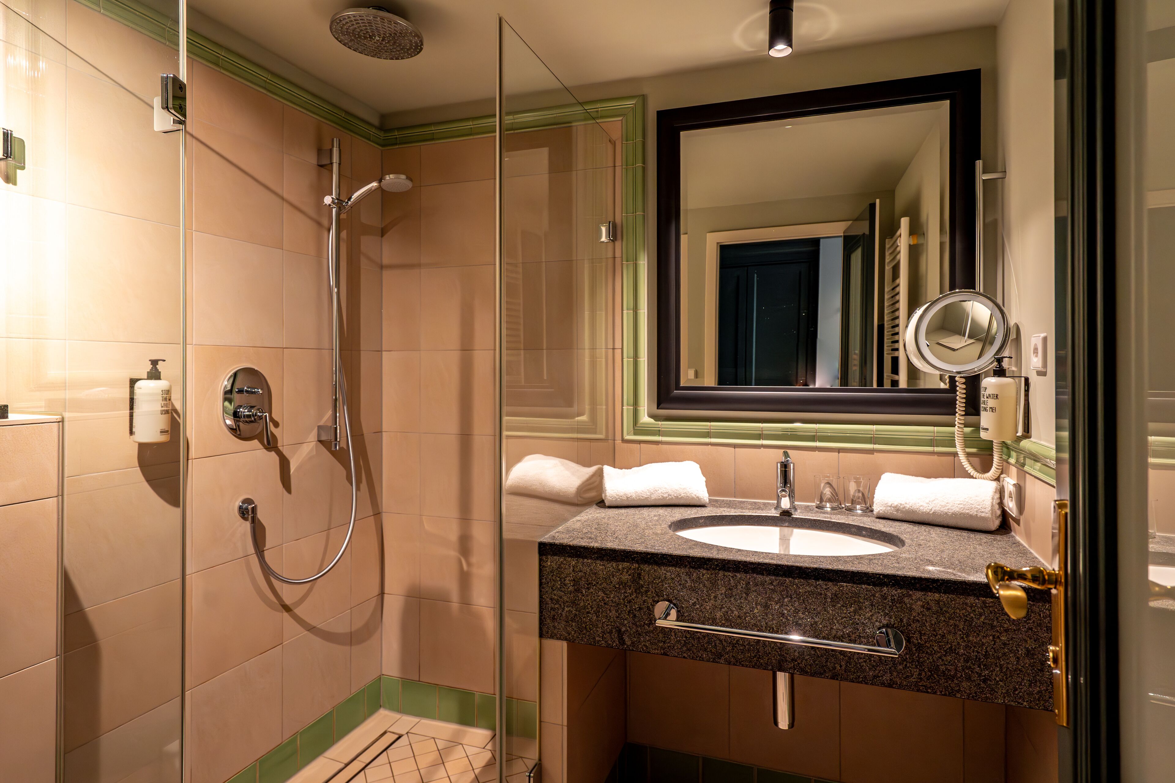 A modern bathroom with a glass-enclosed shower, a sink with a towel rack, and a large mirror.
