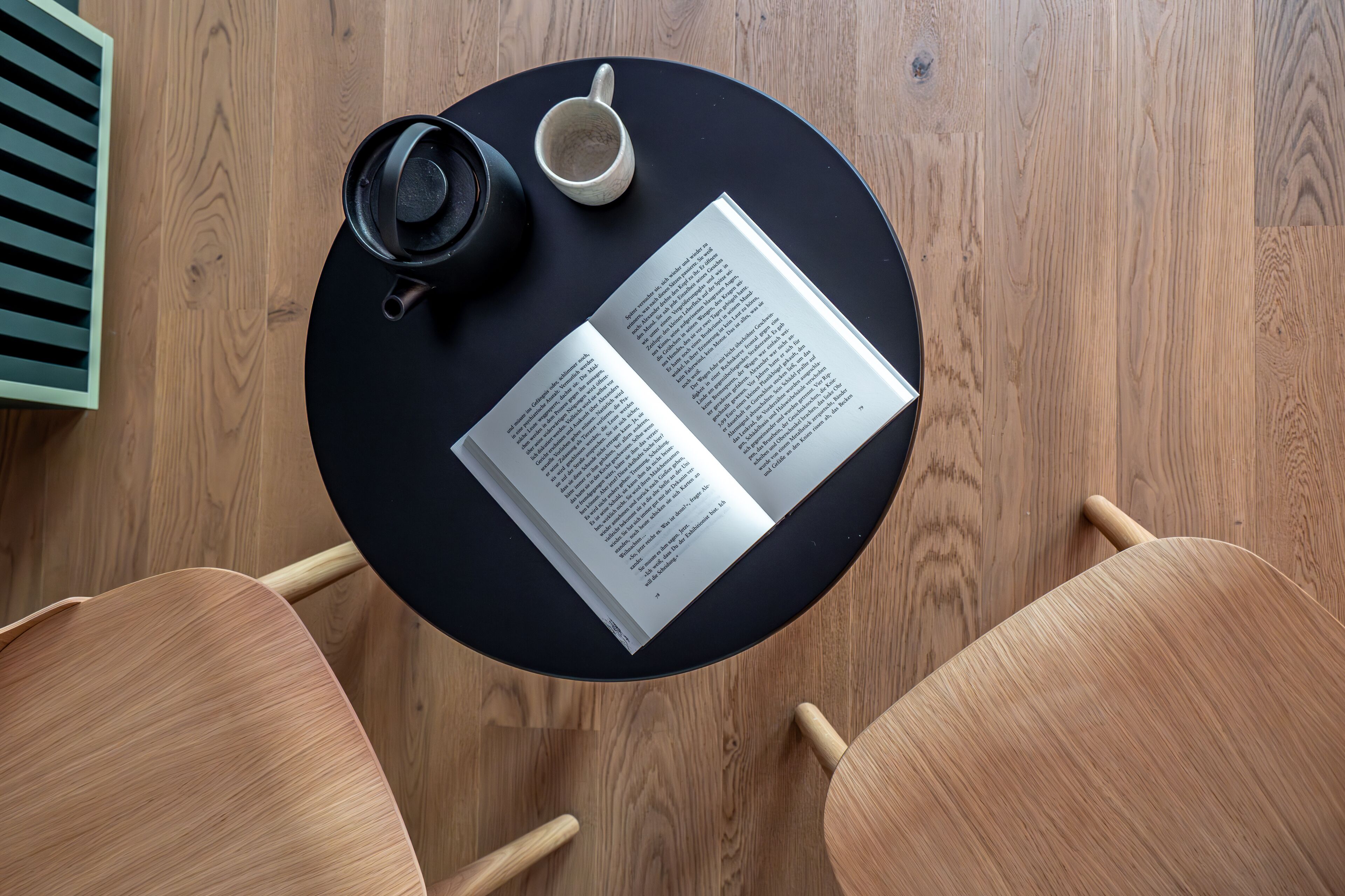 Ein runder Tisch mit einem Buch, einer Tasse und einer Kaffeetasse auf Holzdielen.