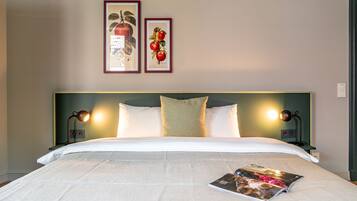 Een net opgemaakt bed met witte lakens, twee ingekaderde foto's aan de muur en een tijdschrift op het bed.