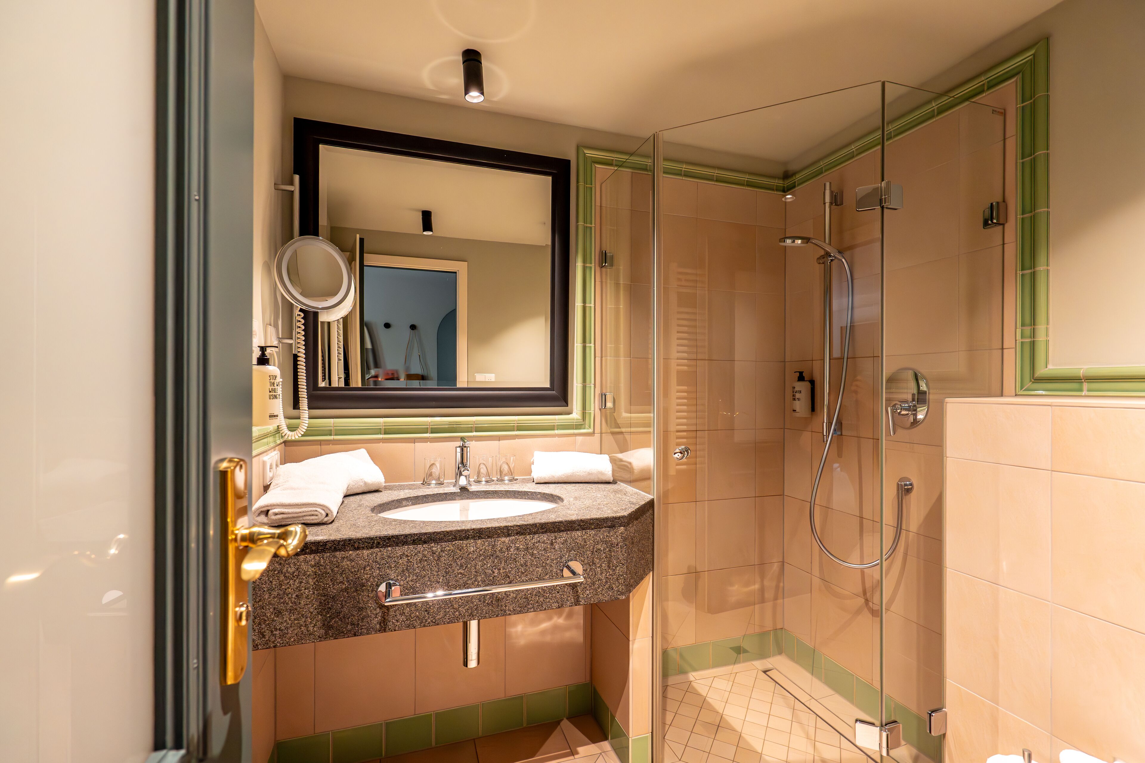 A bathroom with a granite sink, a mirror, a shower, and a glass door.