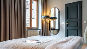 A bedroom with a bed, a window, curtains, a door, and a wall-mounted mirror. - Hotel Deville Staufen (Staufen im Breisgau)