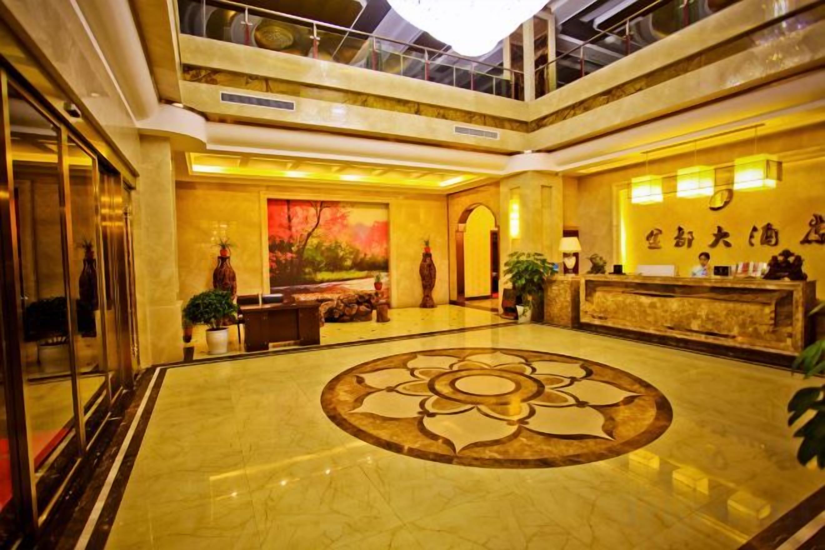 A hotel lobby with a reception desk, a large decorative floor pattern, and a high ceiling with skylights.