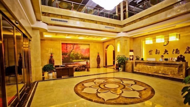 Um hall de hotel com um amplo design floral no chão, uma recepção e uma pintura de árvores.