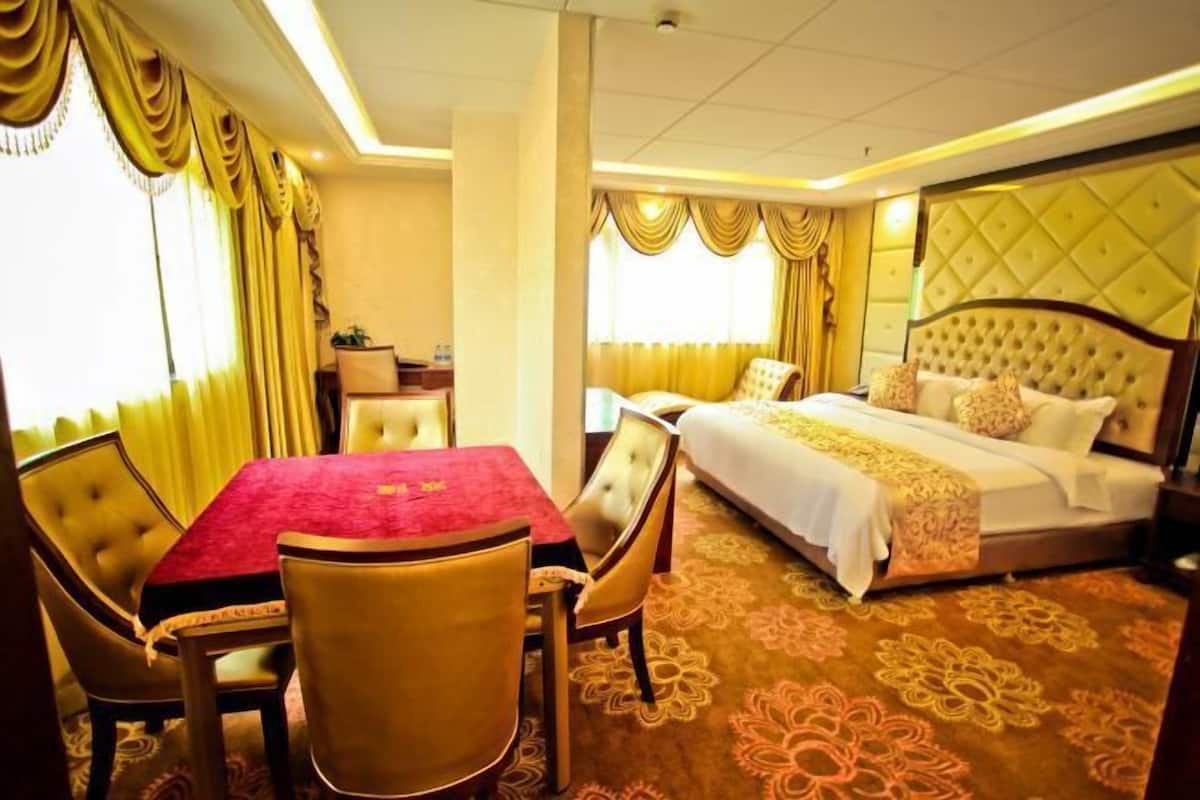 Una habitación de hotel con una cama, una mesa de comedor con sillas y una mesita de noche con lámpara.