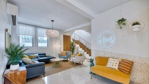 A modern living room with a sofa, armchairs, and a coffee table. There is a staircase leading to another level, and a neon sign on the wall.