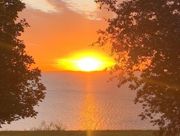 Un coucher de soleil sur une étendue d’eau, avec des arbres encadrant le paysage.