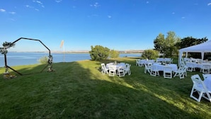 An outdoor wedding setup with a tent, tables, and chairs arranged on a grassy area with a view of a lake. - Cottage on the Lake (American Falls)