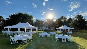 An outdoor event with white tents and round tables set up on a grassy field. - Cottage on the Lake (American Falls)