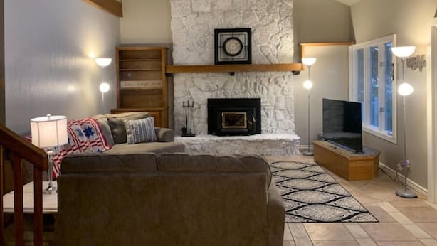 A living room with a stone fireplace, a sofa, a TV, and a bookshelf. - Cottage on the Lake (American Falls)