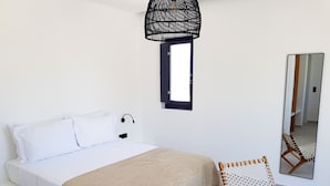 A bedroom with a bed, bedside table, and a chair. - Luxury hospitality, outstanding view (Thira - Santorini)