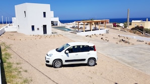 A modern white building with a pool, a covered outdoor seating area, and a view of the sea. - Luxury hospitality, outstanding view (Thira - Santorini)