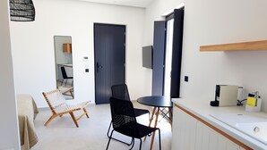 A modern, well-lit room with a dining area, a black chair, a white chair, a small round table, and a kitchen counter with a sink and a towel dispenser. - Luxury hospitality, outstanding view (Thira - Santorini)