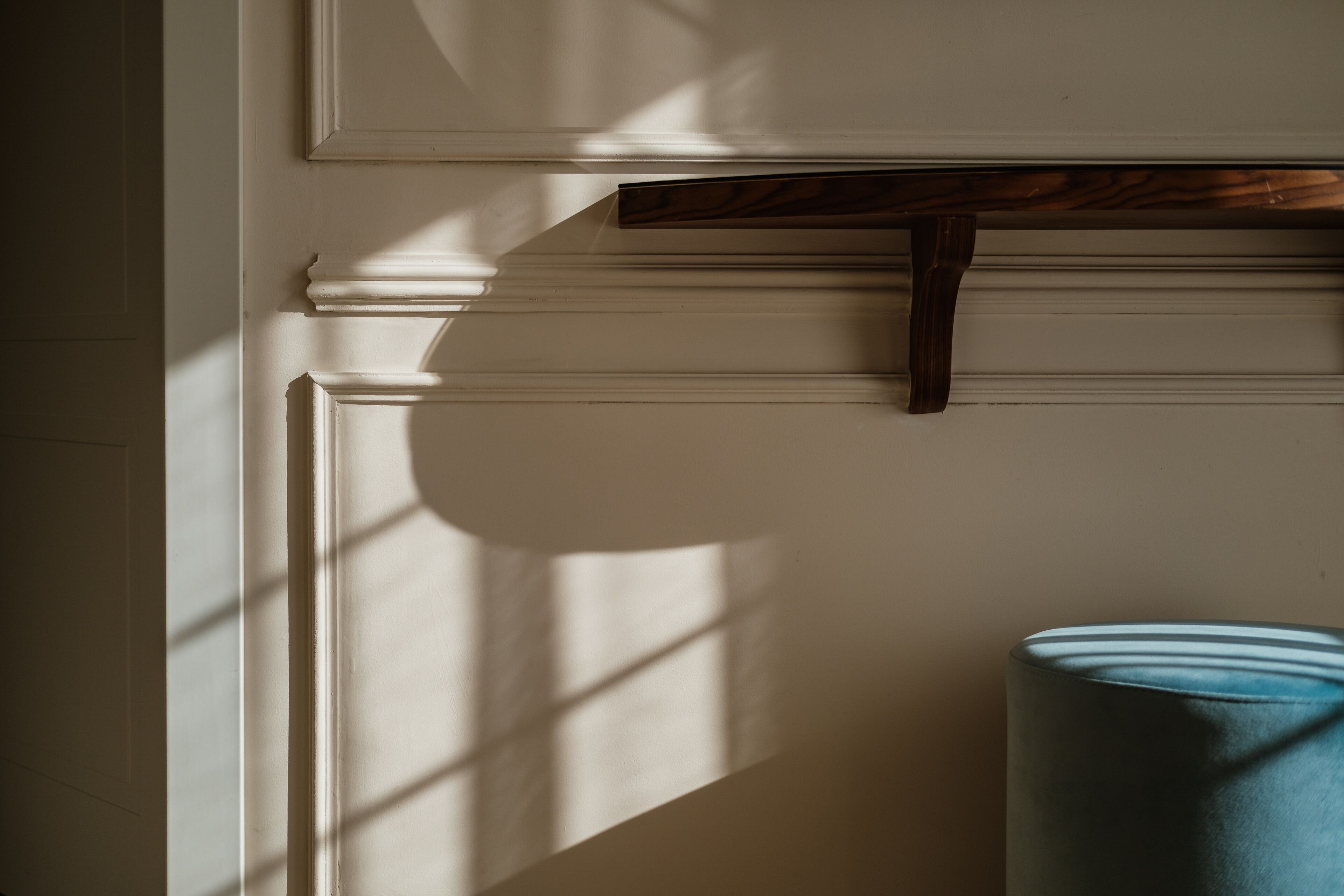 A room with a white wall, a wooden shelf, and a rolled-up blue mat on the floor.