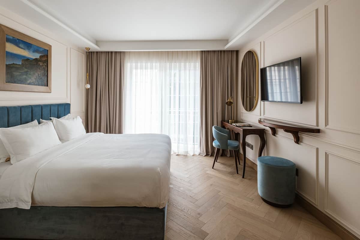 A hotel room with a large bed, a desk with a chair, a television, and a painting on the wall.