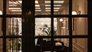 A view through a window with a geometric pattern, revealing a well-lit interior with a staircase, a dining area, and a decorative fountain. - Palazzo Castagna (Ghaxaq)