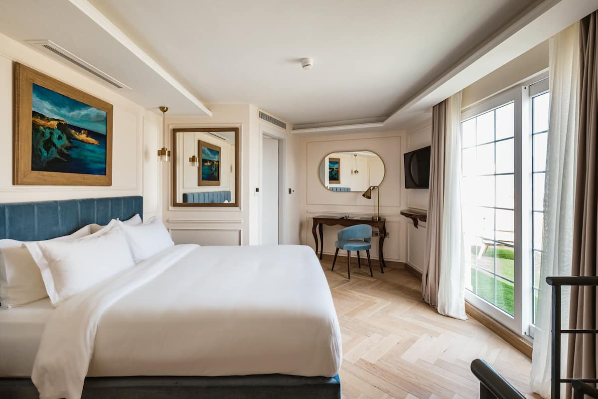 A hotel room with a large bed, a desk, a chair, a television, and a large window with curtains.