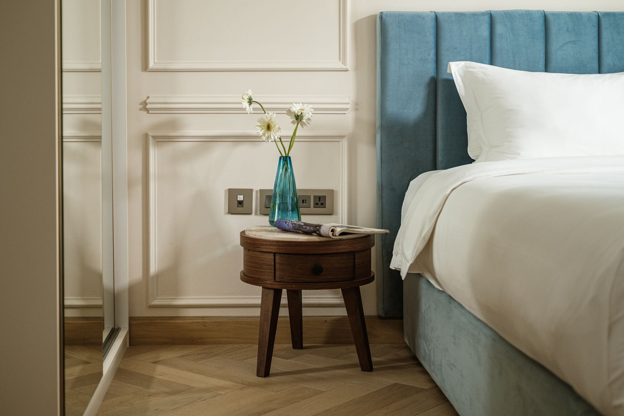 A bedroom with a bed, a nightstand, a vase with flowers, and a wall socket.