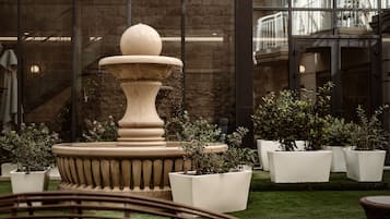 Una fuente de diseño escalonado, rodeada de plantas en macetas y un área con césped.