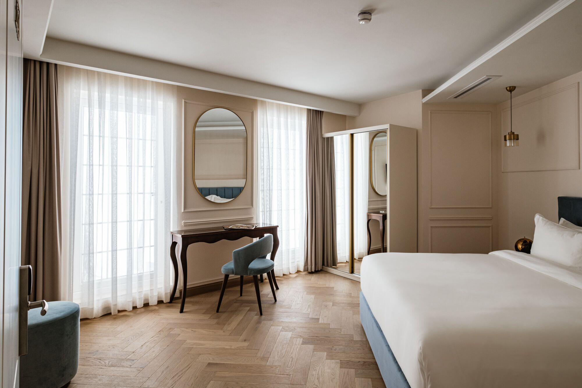 A hotel room with a large bed, a desk with a chair, a large mirror, and a wardrobe.