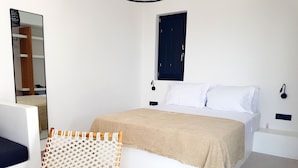 A bedroom with a bed, a macrame chair, a bedside table, and a mirror. - Luxury hospitality, outstanding view (Thira - Santorini)